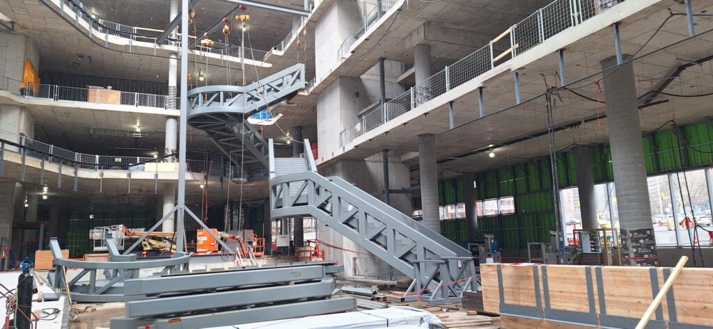Two steel staircases on the inside of the Ādisōke facility under construction, going from the ground floor to the second floor, and from the second floor to the third floor.